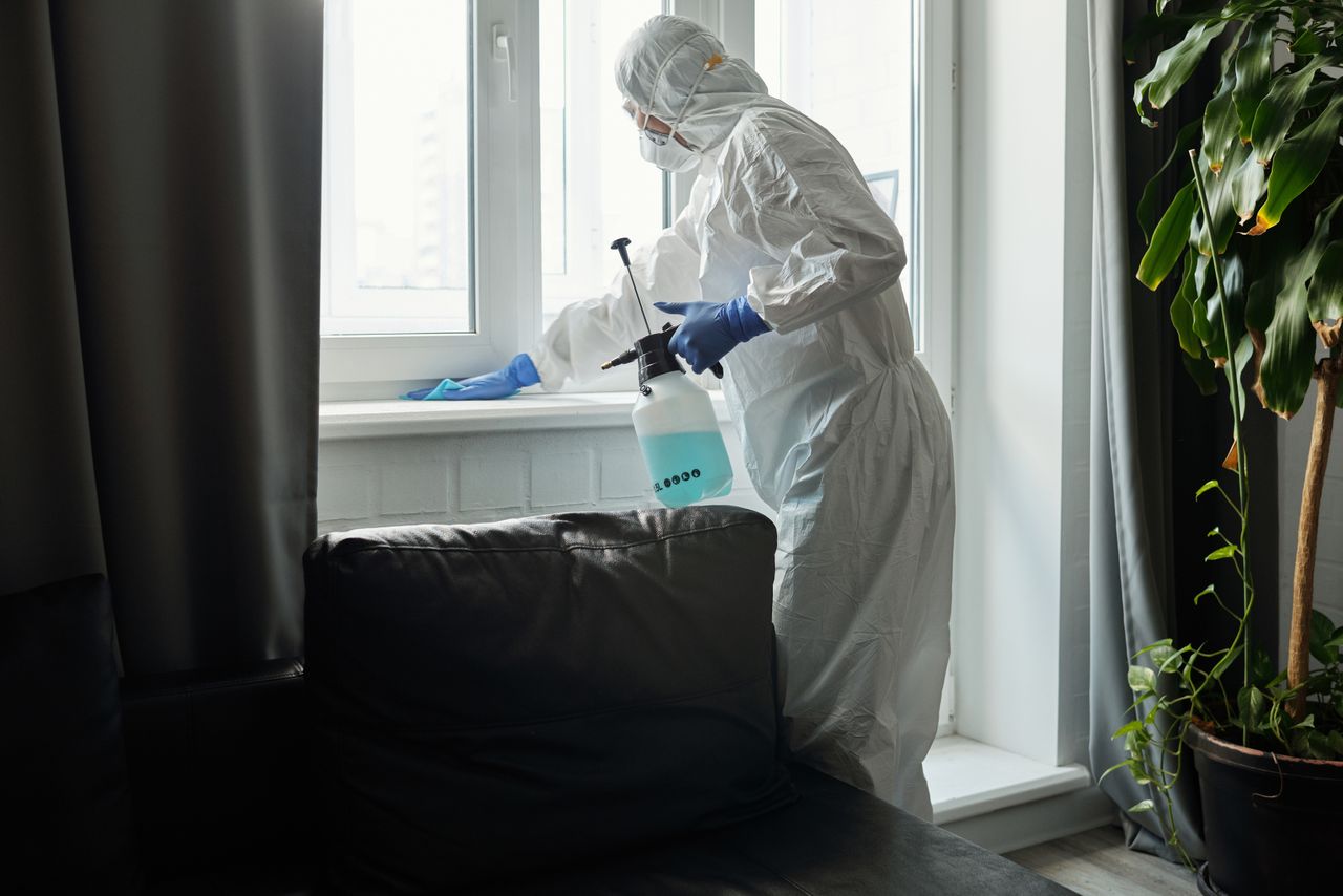 Personne en EPI désinfectant une zone de fenêtre intérieure pendant la pandémie de COVID-19.